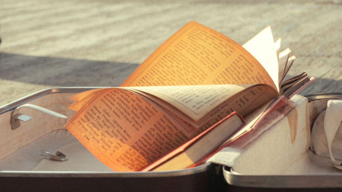 Отворена книга върху куфар на слънчева крайбрежна улица